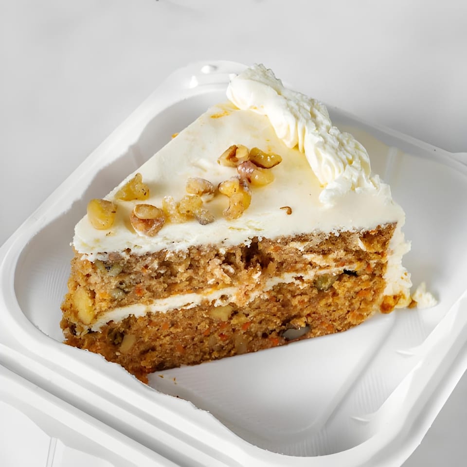 A slice of carrot cake with white frosting and walnuts on a white plate.