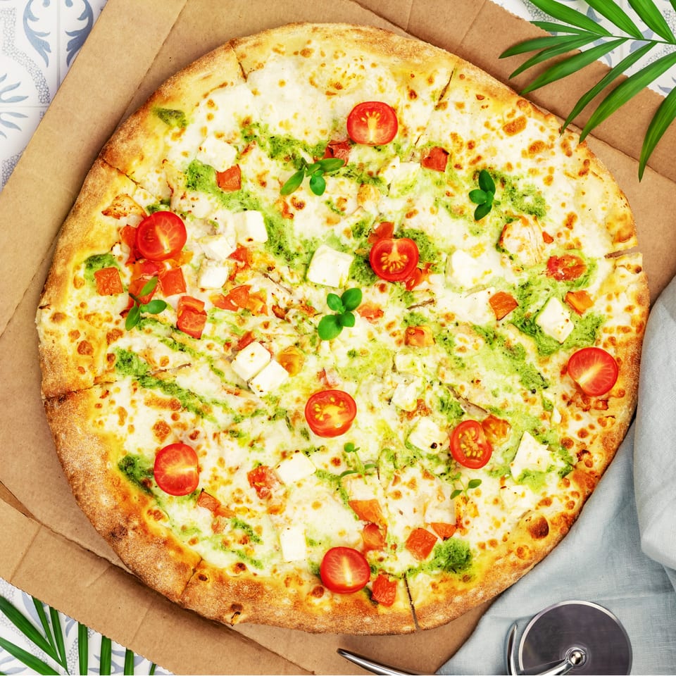 Massey's Pizza with white sauce, pesto, cherry tomatoes, and feta cheese in a pizza box.